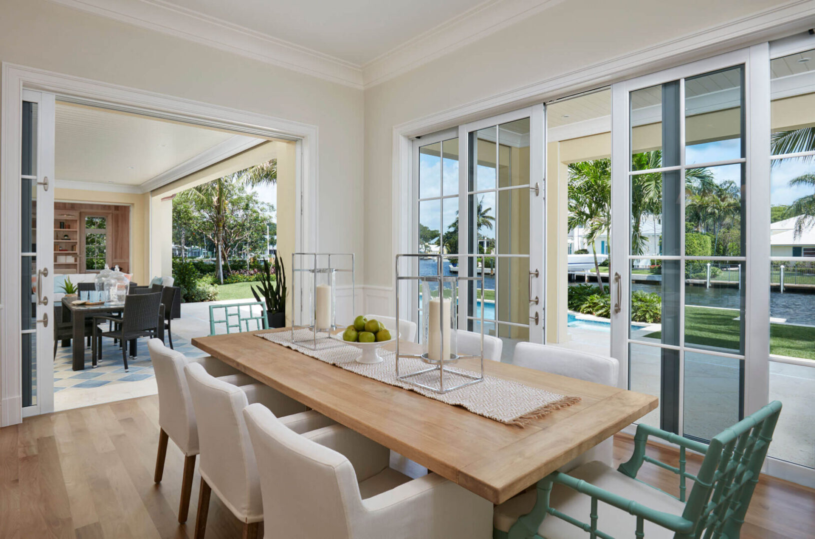 A dining room table with white chairs and a pool in the background.