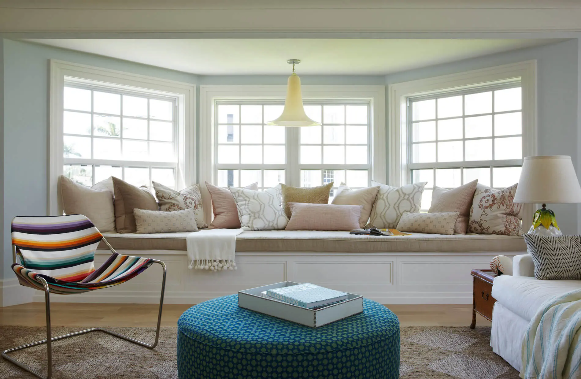 A living room with large windows and a blue ottoman.