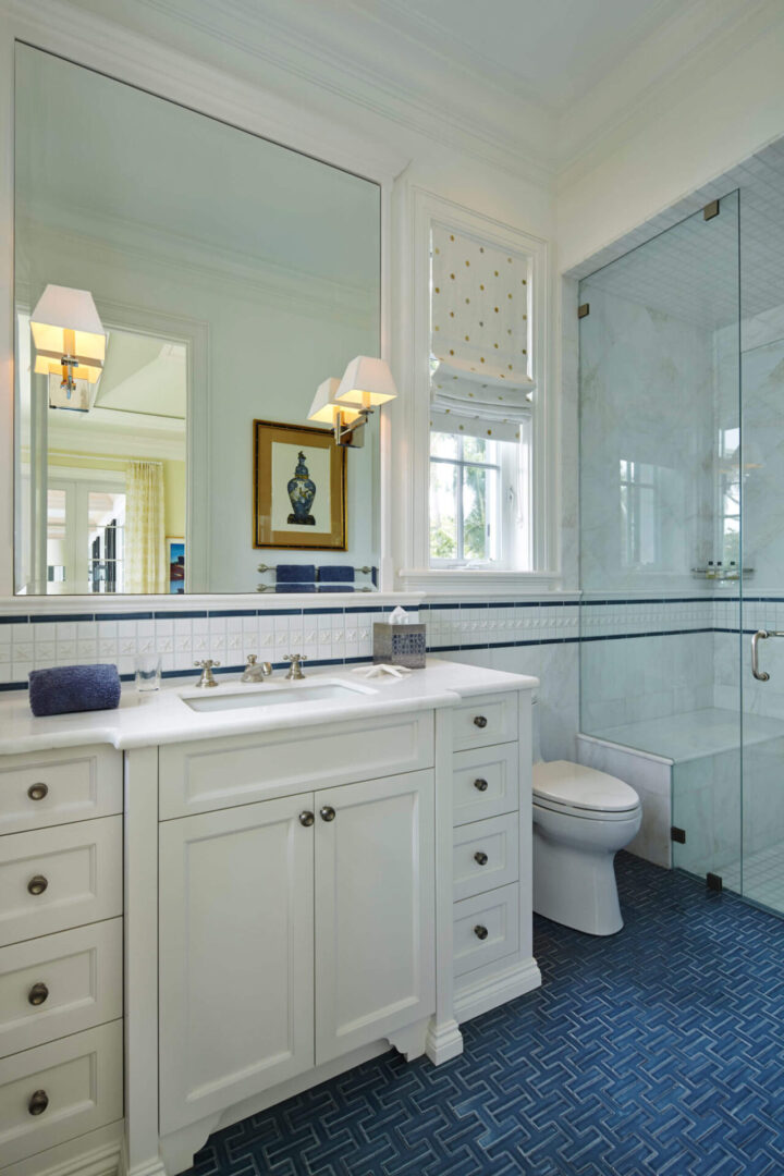 A bathroom with white cabinets and blue tile floor.
