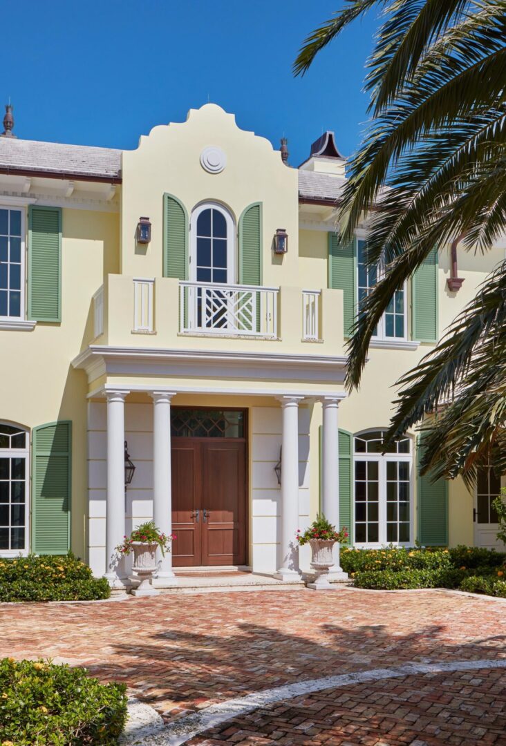A large white house with green shutters and palm trees.
