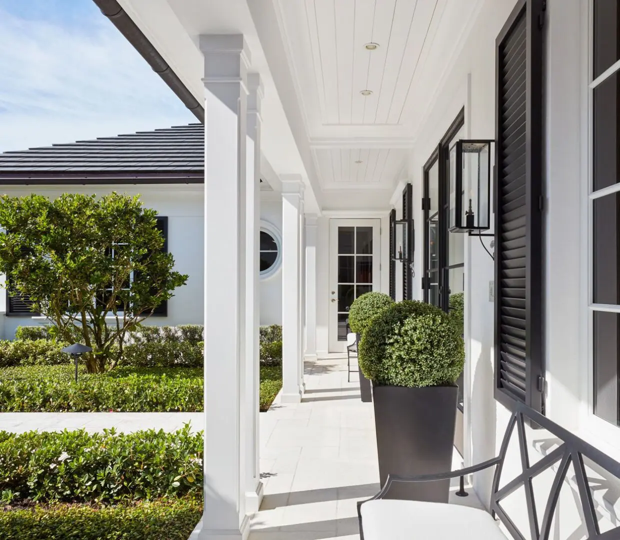 A white porch with black shutters and a large planter.