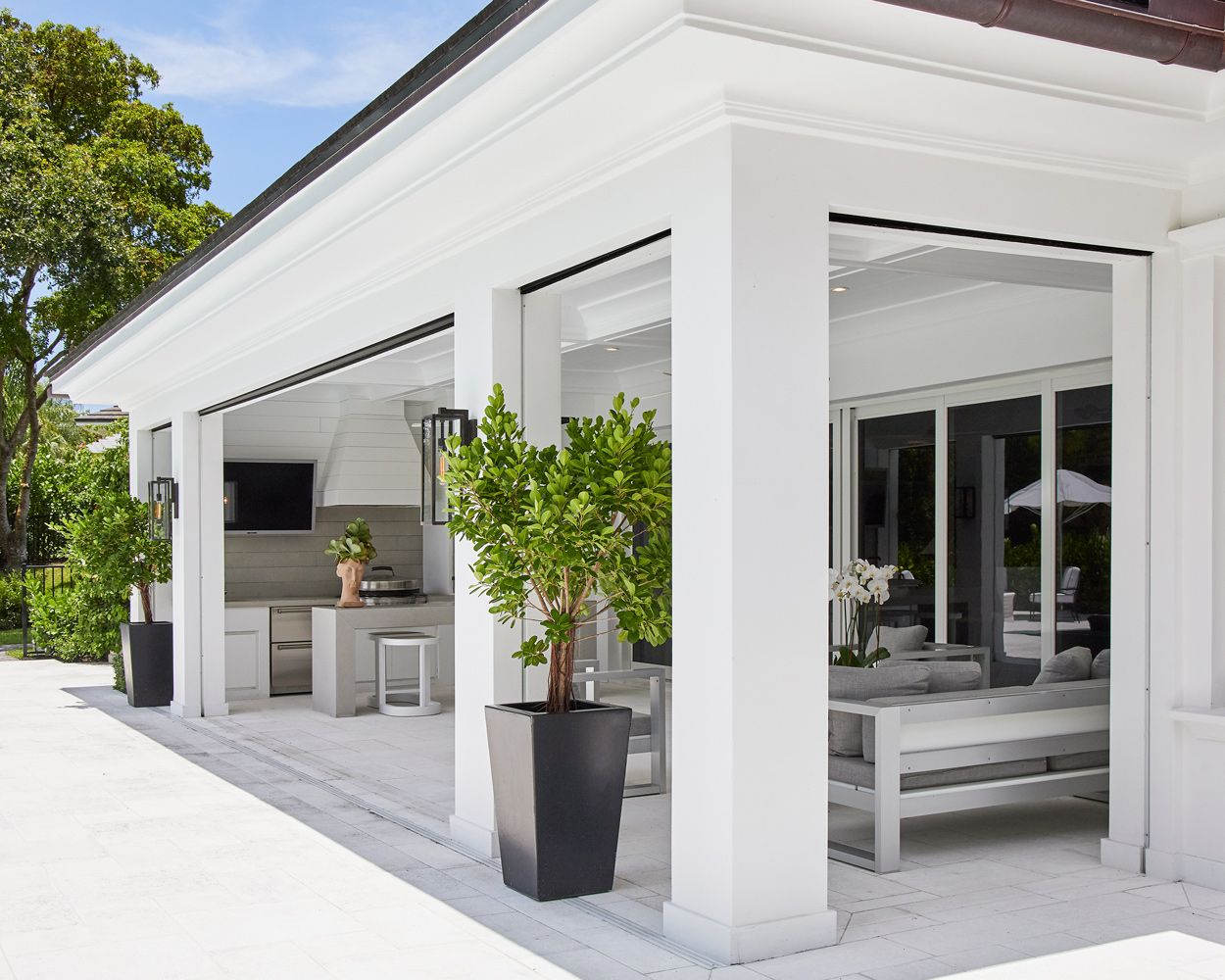 A patio with white pillars and potted trees.