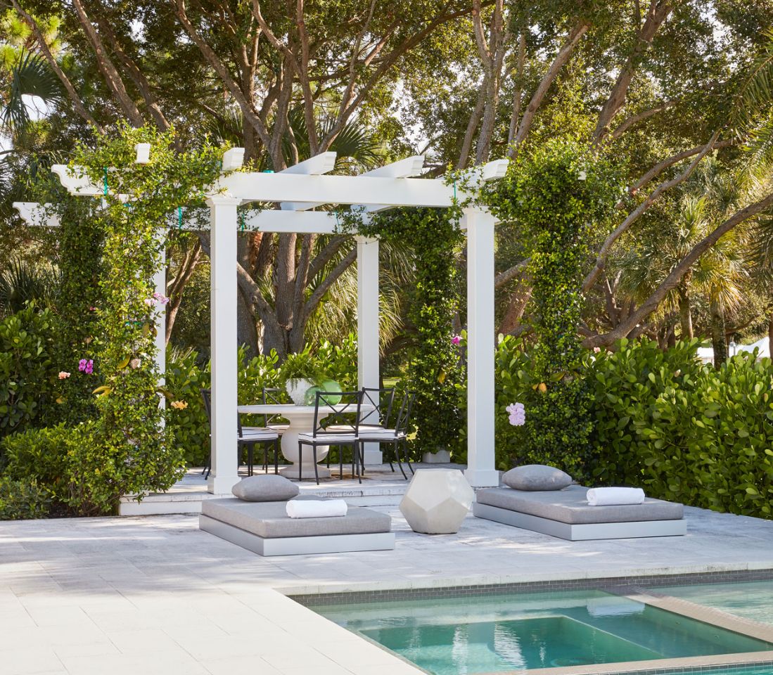 A white gazebo with chairs and tables in front of the pool.