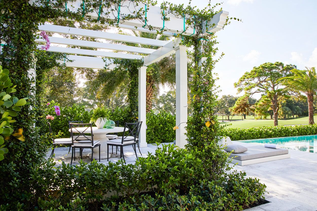 A white pergola with tables and chairs in the middle of a garden.