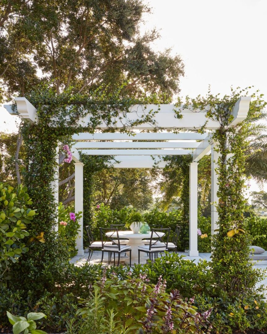 A white pergola with tables and chairs in the middle of a garden.