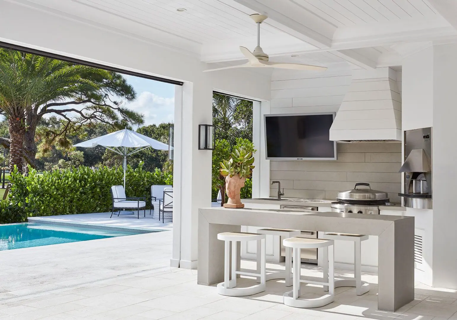 A white outdoor kitchen with an open door to the pool.