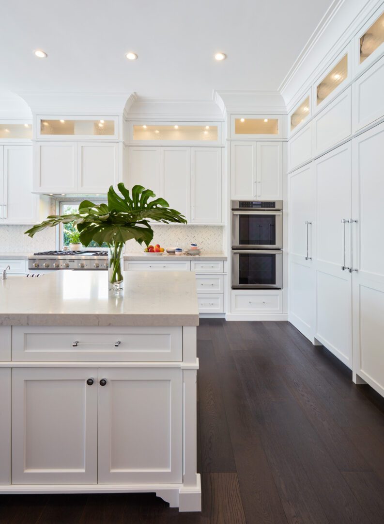 A kitchen with white cabinets and dark wood floors.