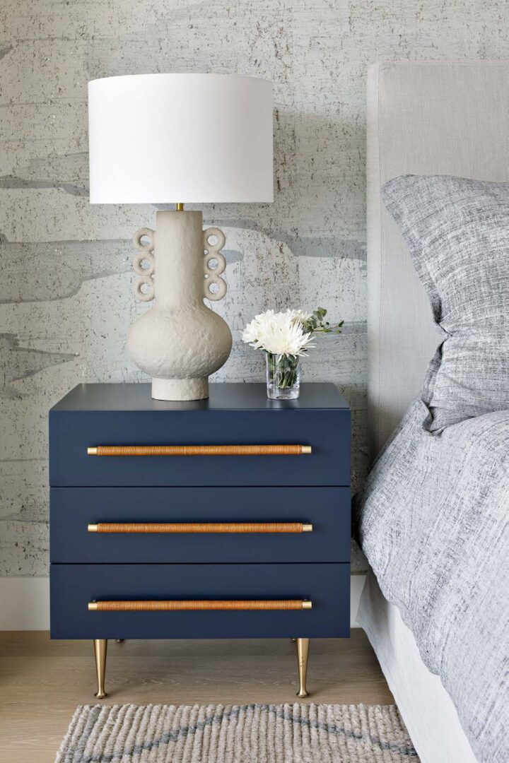A blue nightstand with three drawers and a white lamp.