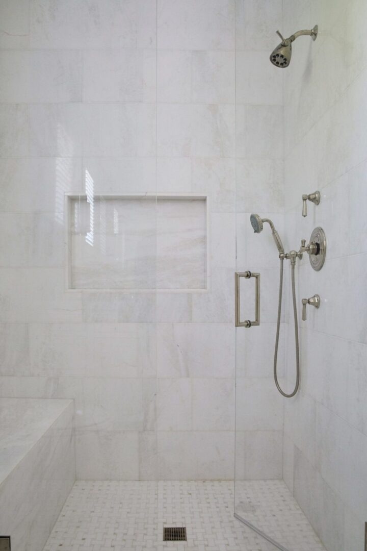 A shower with a glass door and white tile walls.