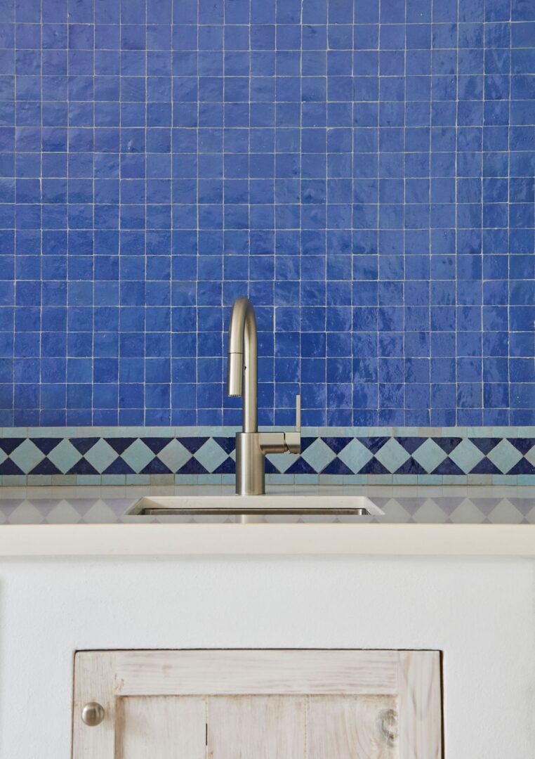 A sink with a blue tiled wall behind it