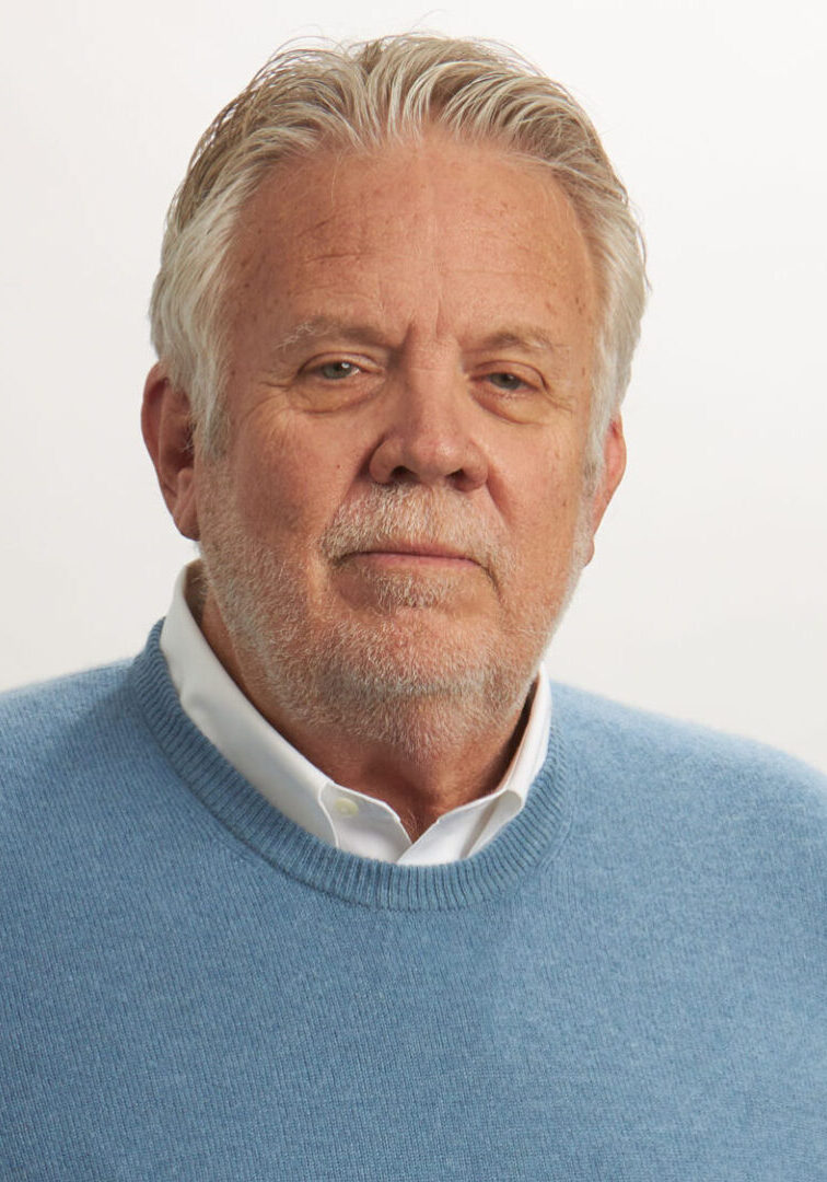 A man with white hair and wearing a blue sweater.
