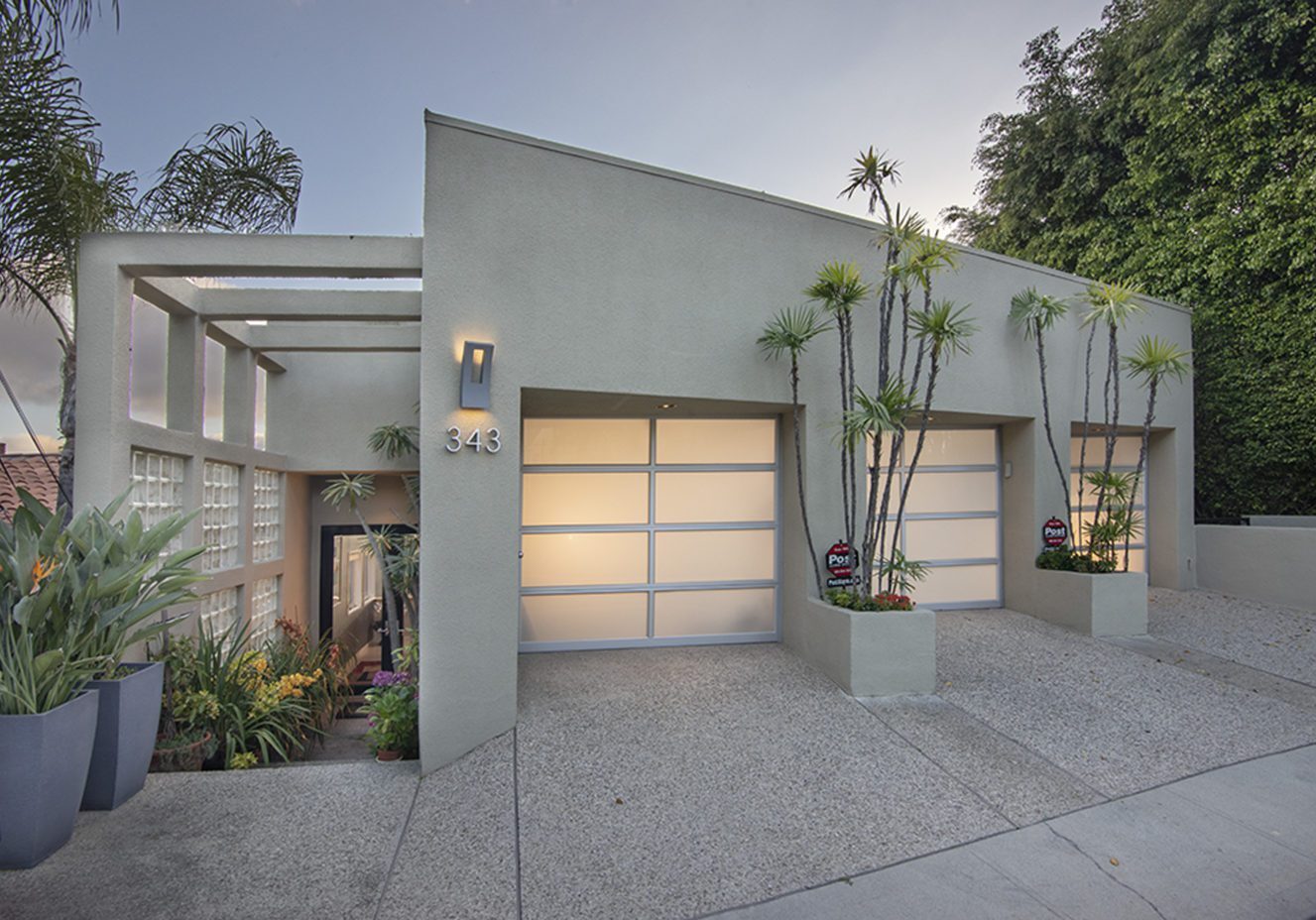 A modern house with two garage doors and plants in the front.
