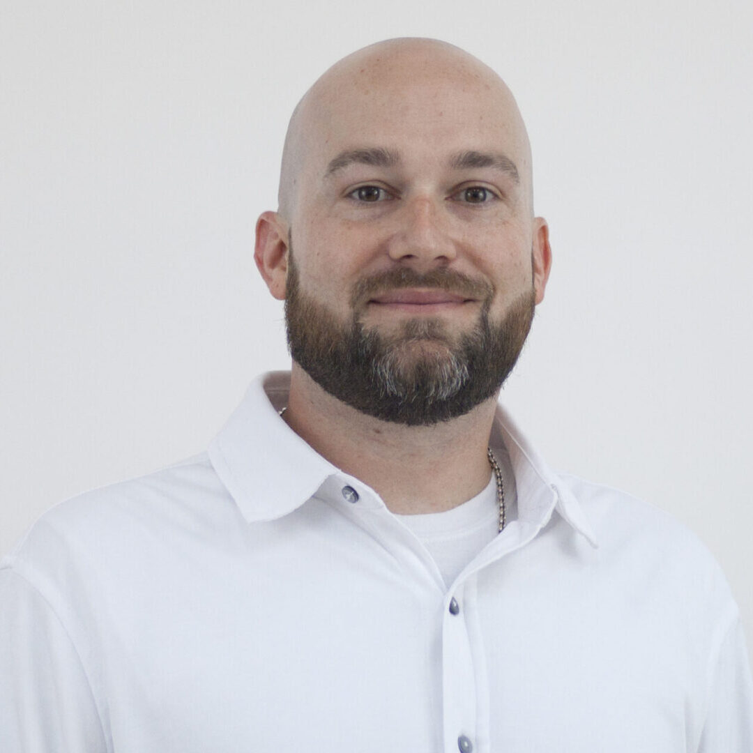 Smiling man with beard in white shirt.